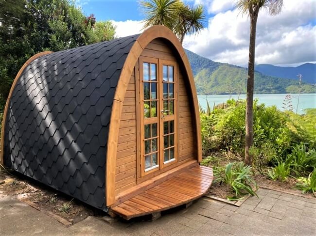 Close-up angled view of Viking Industrier 2.4 x 3.5m camping pod with black shingle roof and dark stained wood frame on a landscaped terrace under daylight.