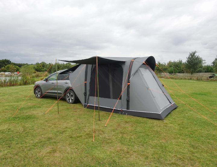 Camptech Adelaide inflatable car tent attached to a silver SUV, featuring a large canopy and orange guy lines on a grassy campsite.