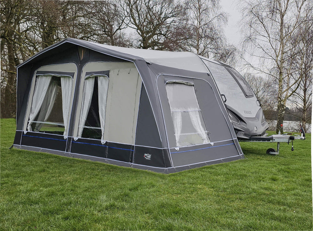 Camptech Archduke awning attached to a caravan, showing large front and side windows with white curtains and modern grey and black design on a grassy pitch.