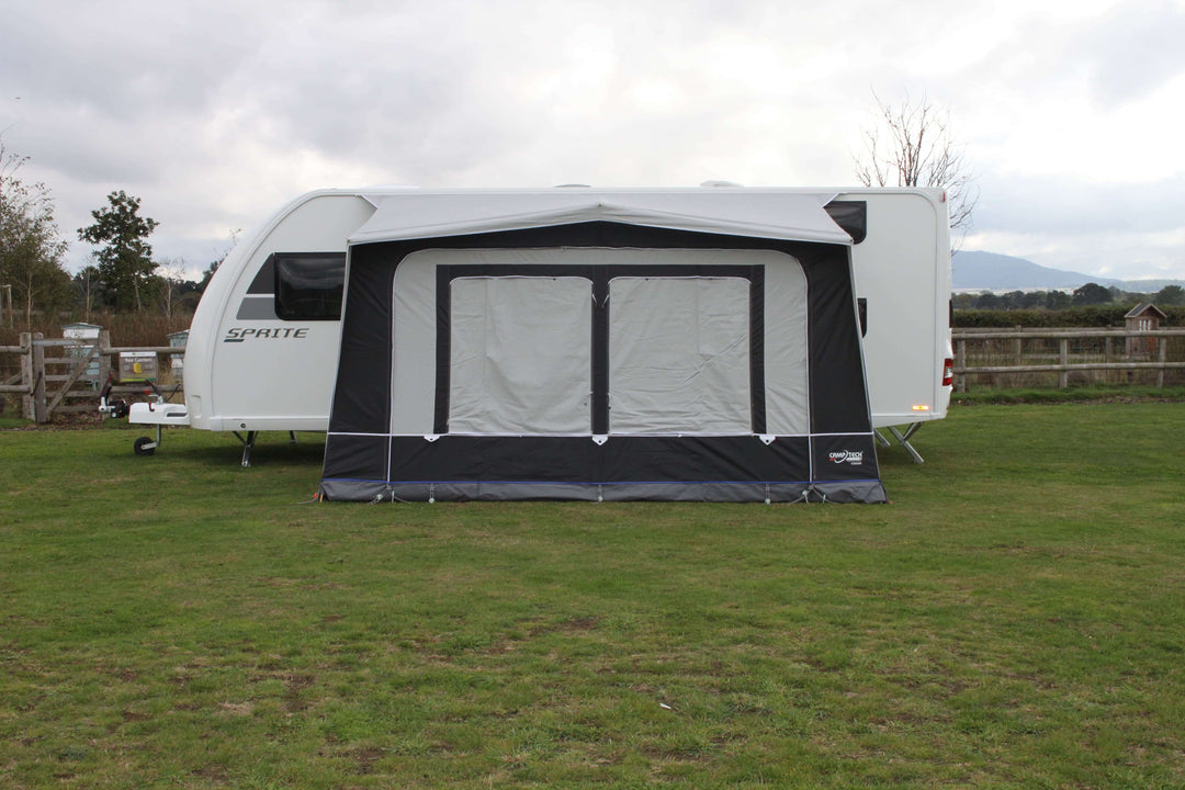 Camptech Count DL porch awning attached to a Sprite caravan, showing closed window blinds on a grassy campsite with cloudy weather.