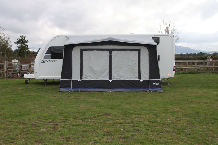 Camptech Count DL porch awning attached to a Sprite caravan, showing closed window blinds on a grassy campsite with cloudy weather.