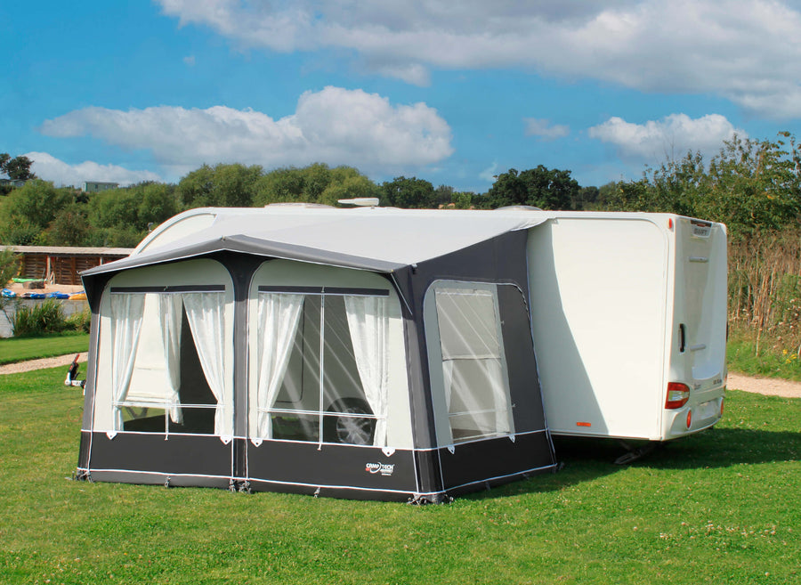 Camptech Duchess 340 porch awning with white patterned curtains and clear windows, attached to a Swift caravan on a green grassy campsite under blue sky.