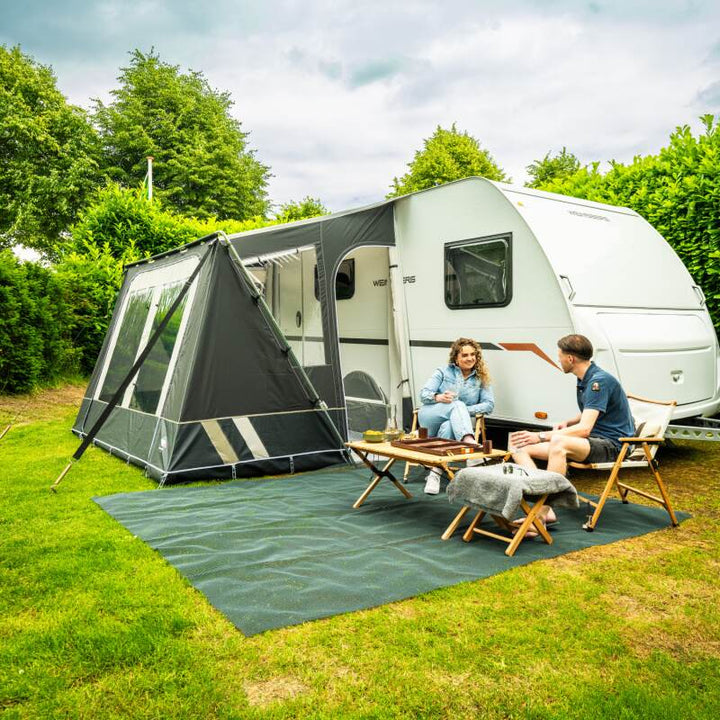 A Dorema Mistral Awning in grey shown from the side in a field with a couple sat on chairs next to it