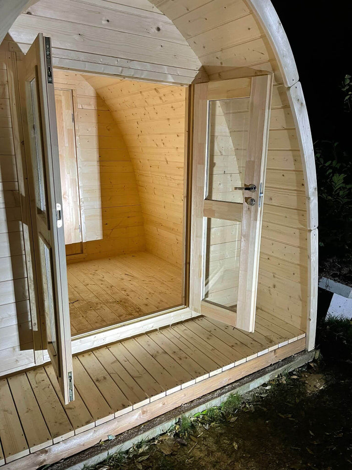 Interior night view of InMedias Camping Pod 480 with doors open, warm lighting, and clean wooden floor and walls.