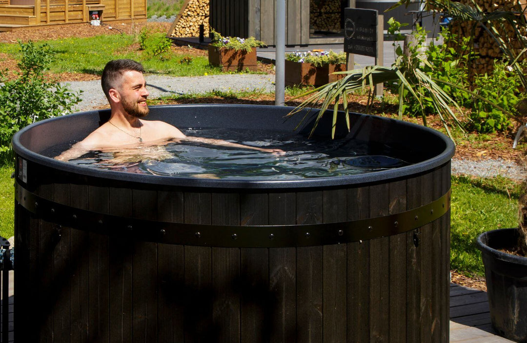 Man enjoying a Harvia Legend wood-fired hot tub in a landscaped garden.
