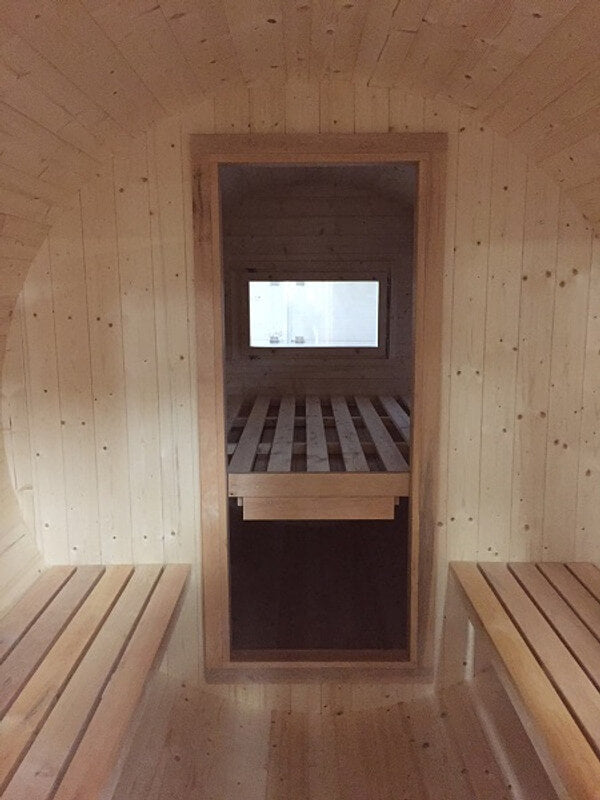 Interior view of the InMedias Camping Barrel 480, showing wooden benches and a windowed partition leading to the sleeping area, on a light brown wooden background.