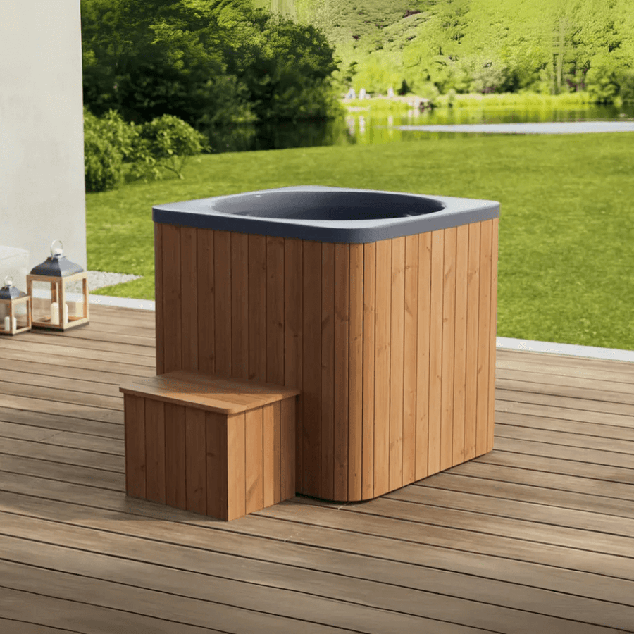 Square wood-panelled cold plunge tub with dark interior and step, placed on an outdoor deck with green landscape in the background.