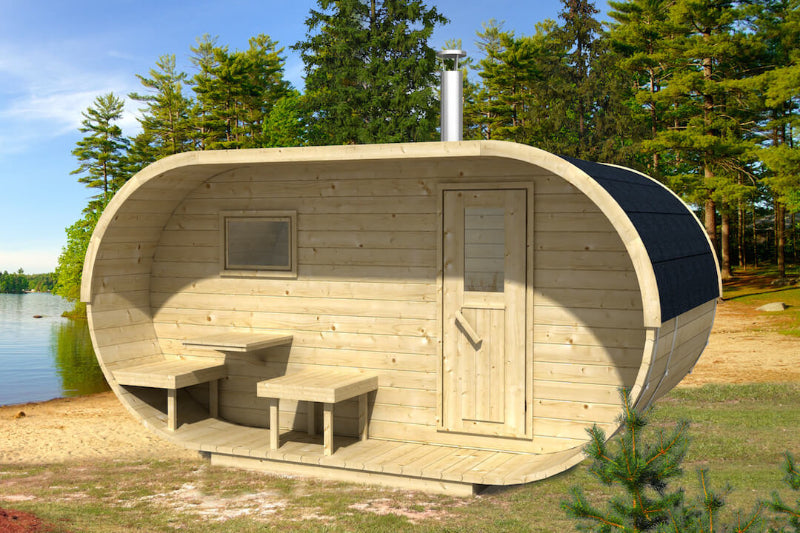 InMedias Oval Sauna on a lakeside grassy beach with light pine wood finish and forest in the background,sunny outdoor setting
