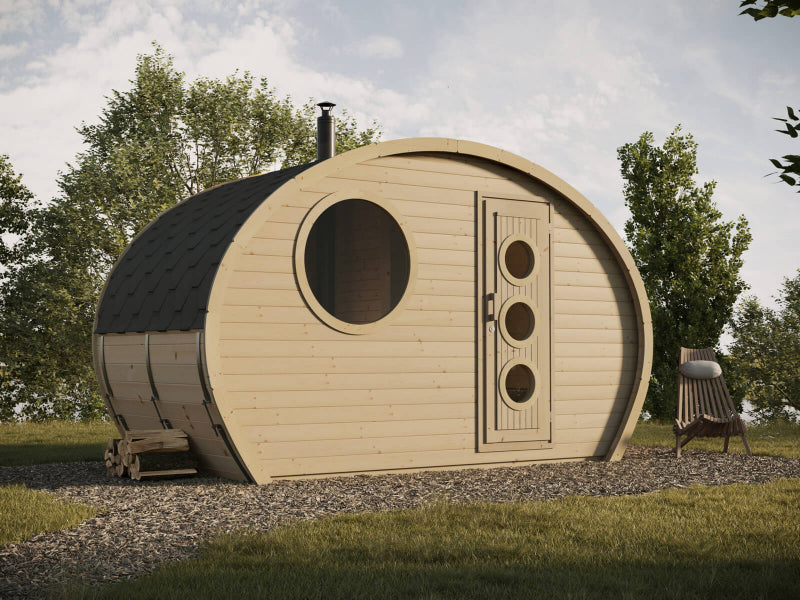 Outdoor view of the InMedias Oval Sauna Frodo 195 in a grassy area with trees and a wooden chair beside it, under a partly cloudy sky.