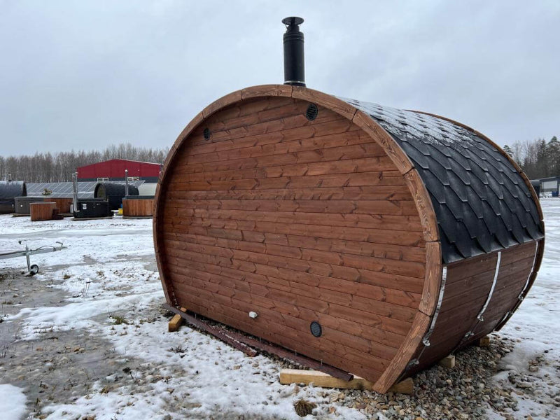 Rear view of the InMedias Oval Sauna Frodo 195 with a dark roof and chimney, placed outdoors on snow-covered ground.
