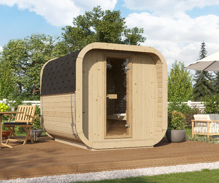 Side angle view of the InMedias Sauna Icon 250S in a residential garden setting with furniture, wooden deck, and sunny weather, with outdoor garden background.