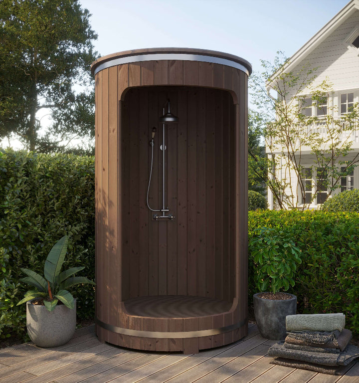 Full outdoor view of InMedias Shower Barrel with mounted black shower system – positioned on a wooden deck with greenery and a house in the background, under a clear sky.