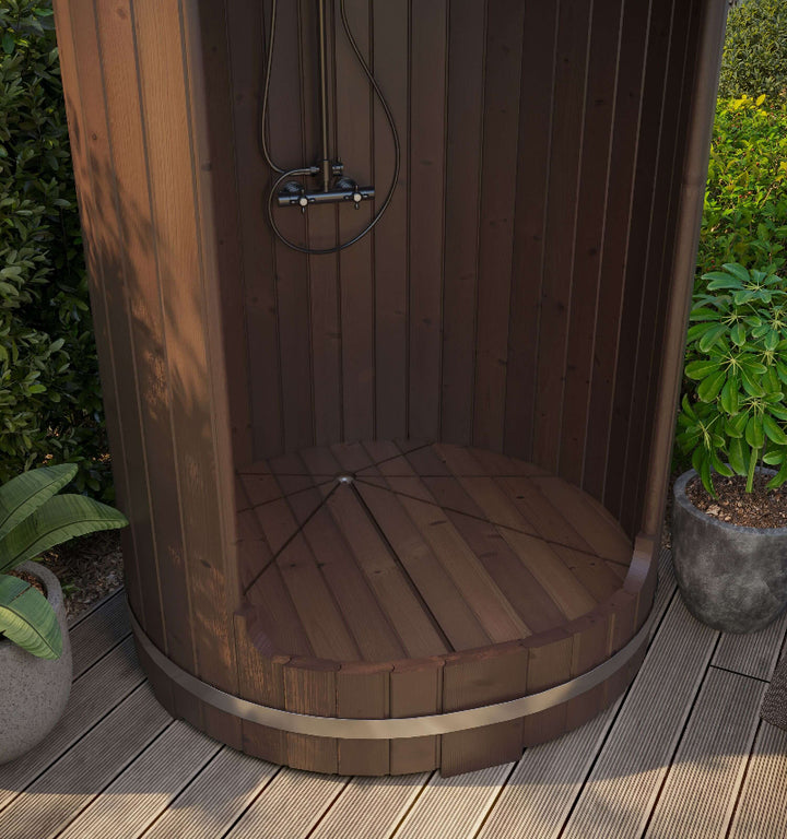 Outdoor view of InMedias Shower Barrel installed on wooden decking – partially shaded, surrounded by potted plants, on a garden background.