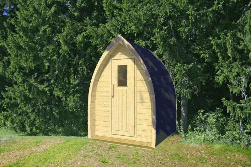 InMedias Toilet Barrel small wooden cabin with a pointed roof and shingled black top, standing on grassy terrain with a forested background – natural daylight, green background.
