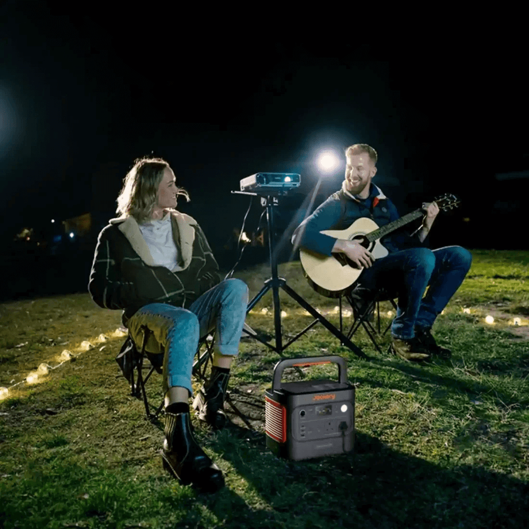 Jackery Explorer 2000 V2 portable power station powering a projector for a night outdoor movie while a couple relax and play guitar.