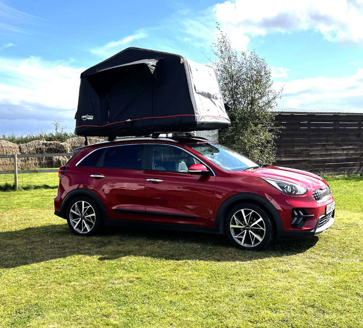 Camptech Queensland inflatable rooftop tent mounted on a red SUV at a campsite, shown with the tent partially opened under a blue sky.