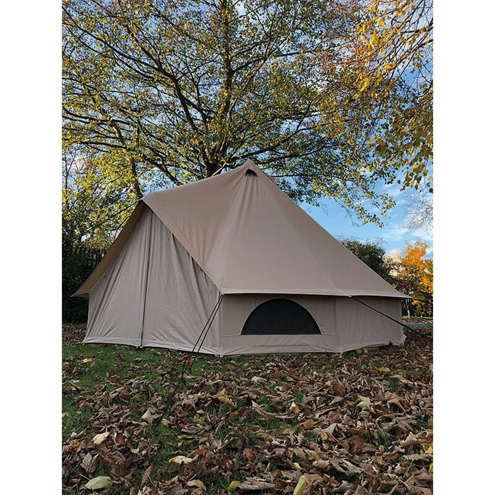 Side view of the Quest Leisure Signature Touareg bell tent with circular window, set up among dry fallen leaves under trees with an autumn sky.