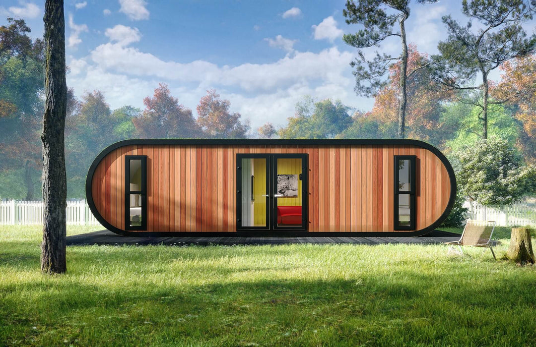 Glamping unit with curved green-covered sides and vertical wood cladding, shown front-facing on a lawn surrounded by trees and a white picket fence.
