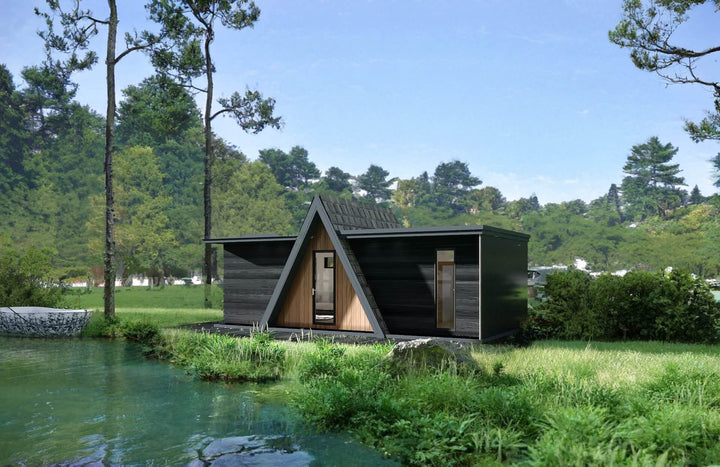 Modern A-frame glamping unit with black and wood exterior, positioned near a small pond surrounded by greenery.
