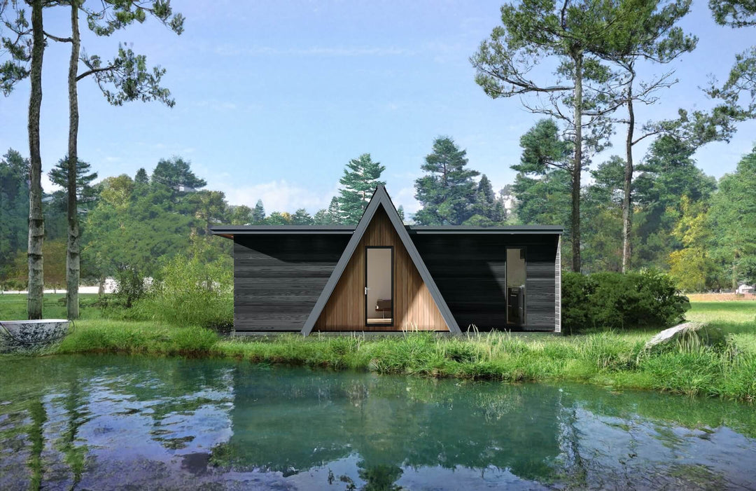 Front-facing view of an A-frame glamping unit reflected in a pond, surrounded by pine trees and forest grass.