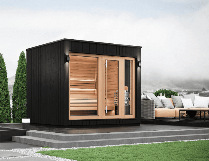 Outdoor setup of the Saunum AirCube One sauna on a modern patio with garden, showing its black exterior and natural wood interior, surrounded by lounge seating.
