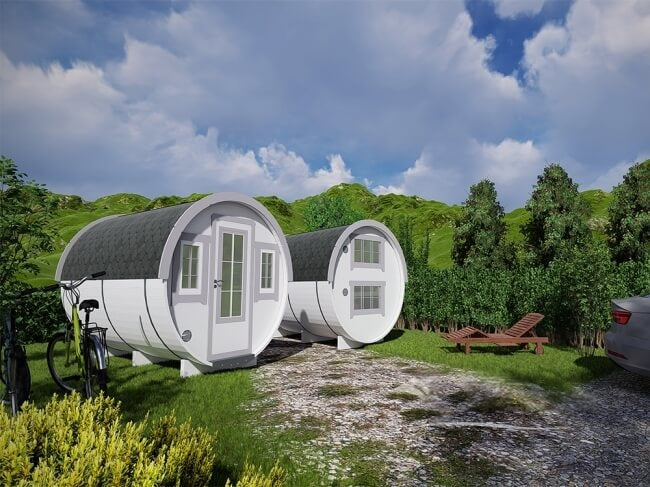 Two Viking Industrier 2.2 x 3.3m Sleeping Barrels placed outdoors on a gravel path surrounded by grass and bushes, under a partly cloudy sky.