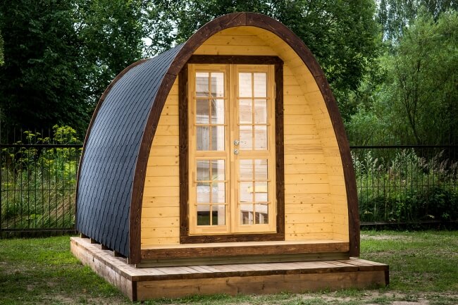 Viking Industrier 2.4 x 4.8m Camping Pod with terrace and dark wood trim in an outdoor setting with trees and grass.