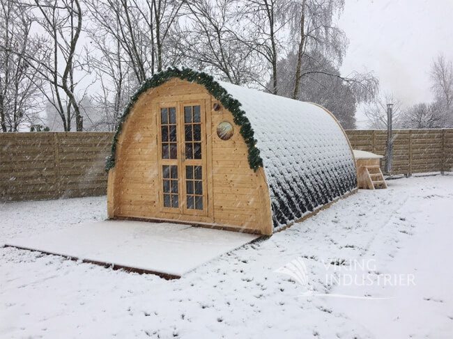 Viking Industrier 2.4 x 5.9m camping pod covered in snow with decorative garland on a snowy outdoor background.