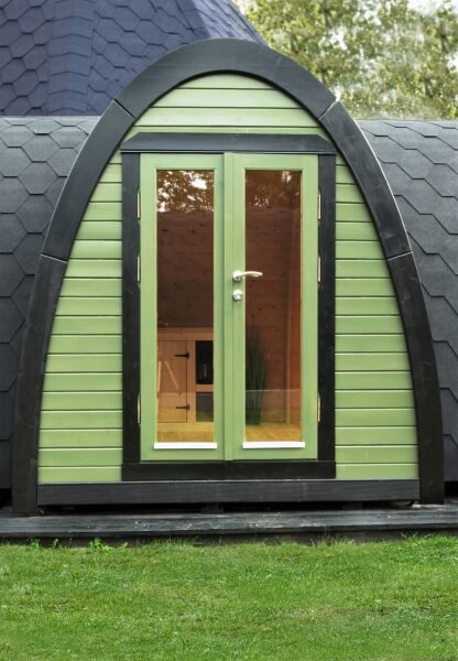 Close-up of green door entrance of the Viking Industrier 2.4 x 5.9m Camping Pod framed by black trim on a grassy outdoor background.