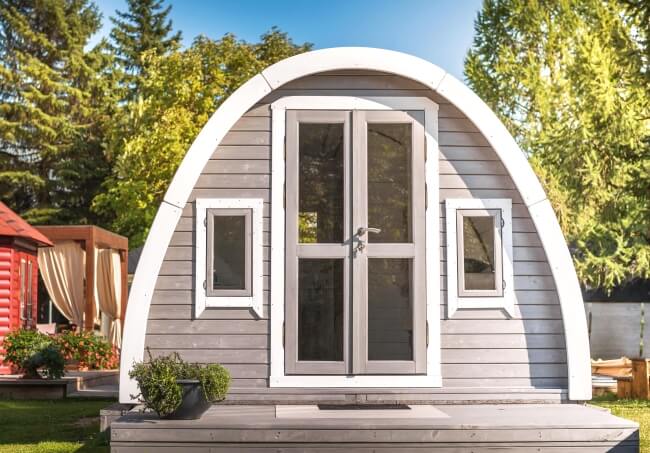 Viking Industrier 3.2 x 5.9m Camping Pod exterior front view with grey siding and double glass doors with white trim on a green garden background.