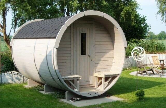 Outdoor photo of a beige Viking Industrier Barrel Sauna 1.9 x 3.5m with dark roof and benches, surrounded by grass.
