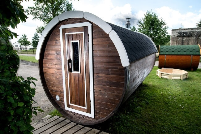 Exterior view of Viking Industrier Barrel Sauna painted in dark wood with white trim, placed on grass with cloudy skies.