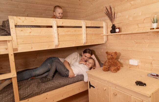 Interior of Viking Industrier Delight Camping Pod 2.4 x 4.3m showing a mother and two children lying on wooden bunk beds with dark gray sheets inside a wood-paneled room.