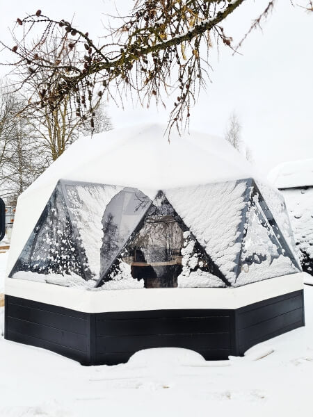 Viking Industrier Glamping Dome 10m covered in snow with a transparent triangular window facade and visible interior, surrounded by trees.