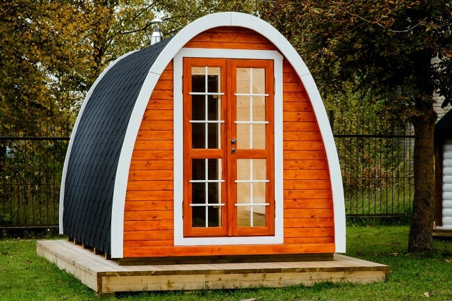Viking Industrier Sauna Pod 2.4 x 4m exterior with orange wood finish, black shingle roof, and white trim, placed outdoors on grass.