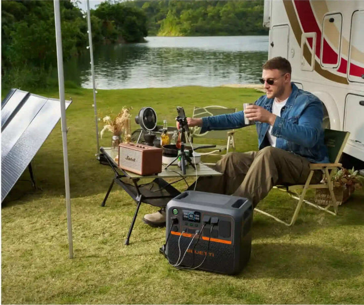 A man sitting by a lakeside RV setup, enjoying coffee while the Bluetti AC200P L powers multiple devices.