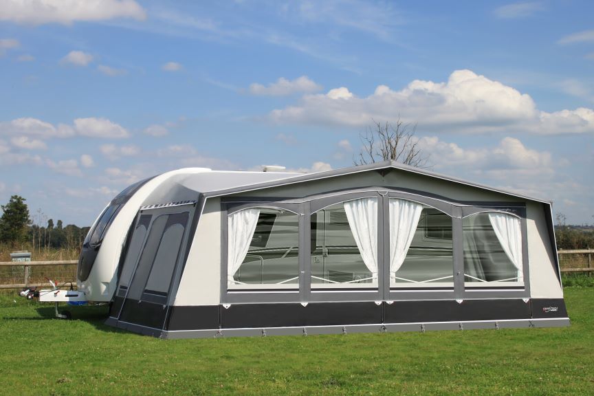 Camptech Buckingham DL full caravan awning with large front windows and white curtains, set up on a green grassy campsite under a clear blue sky.