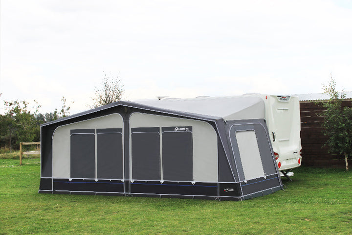 Camptech Savanna DL full awning with all window blinds closed, attached to a white caravan on green grass with trees and fencing in the background.