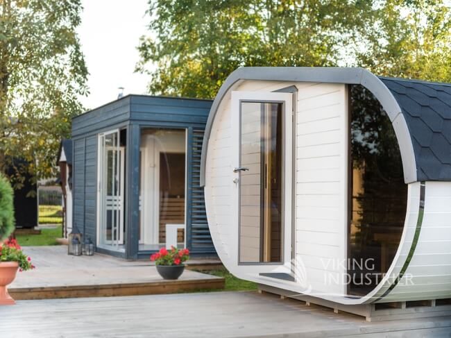 Viking Industrier Delight Outdoor Sauna 2.4 x 4.3m beside a modern glamping pod in a garden on a sunny outdoor background.