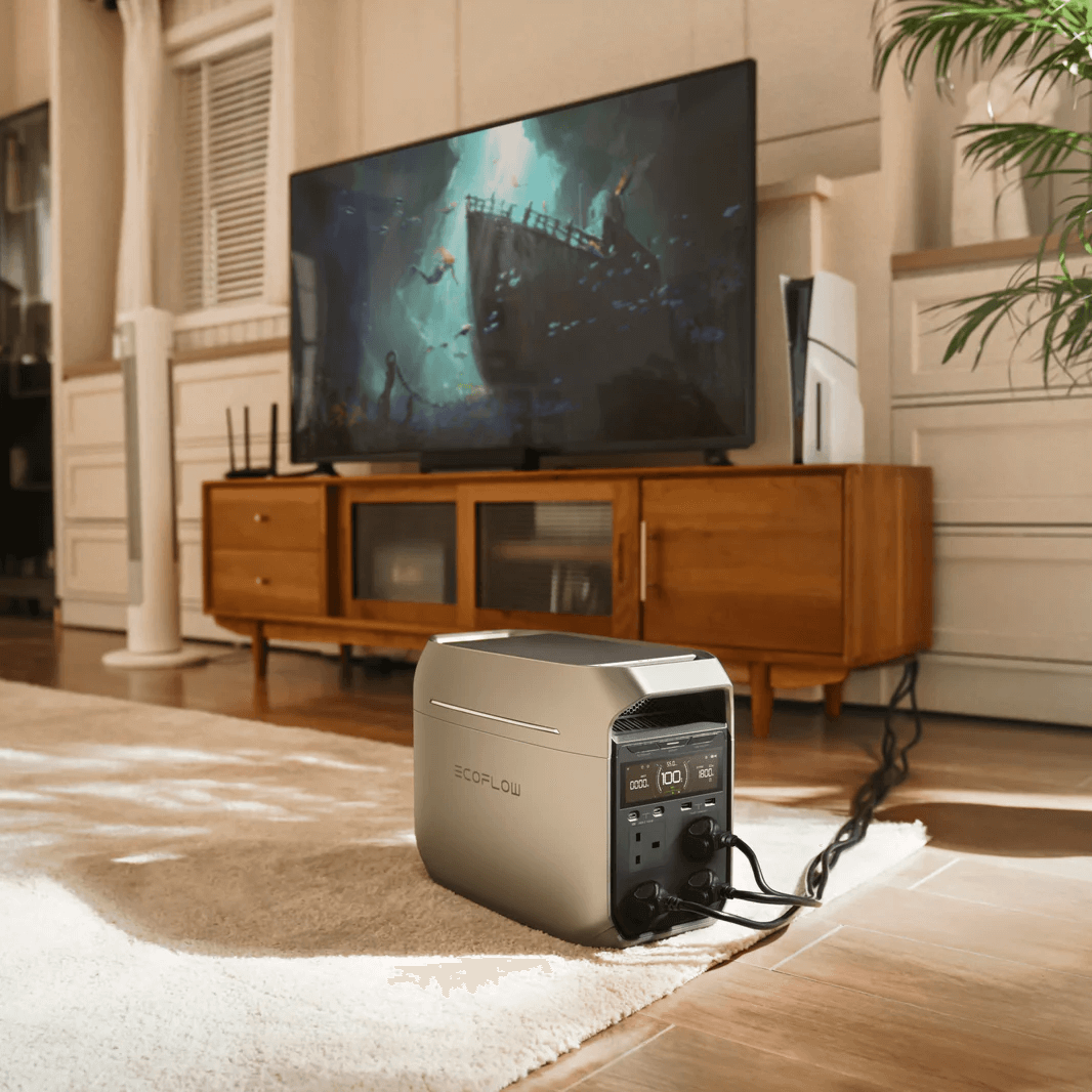EcoFlow DELTA 3 Series power station powering a television in a cozy, modern living room with wooden furniture, a large TV screen showing an underwater scene, and warm indoor lighting.