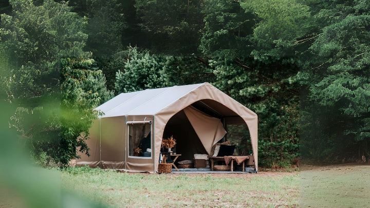 FDomes Glamping Tent in a forest clearing – a tan canvas glamping tent set up in front of lush green trees, surrounded by grass and natural foliage, on a natural background.