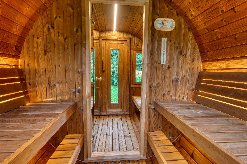 Interior view of InMedias Barrel Sauna 400 Deluxe showing wooden benches, wall thermometer, and view through changing area toward front door.