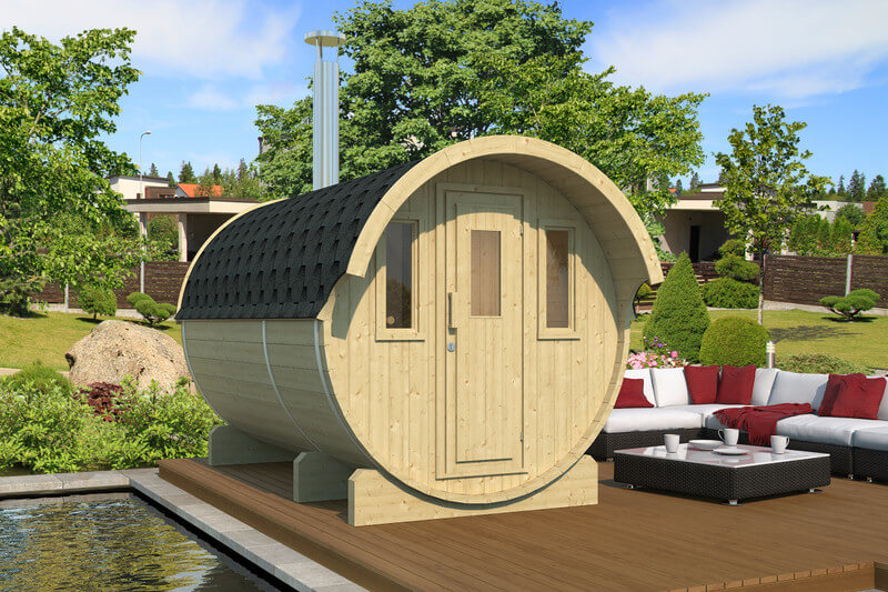 InMedias Barrel Sauna 330 in light wood finish placed on a deck beside red and white outdoor furniture — on a garden background.