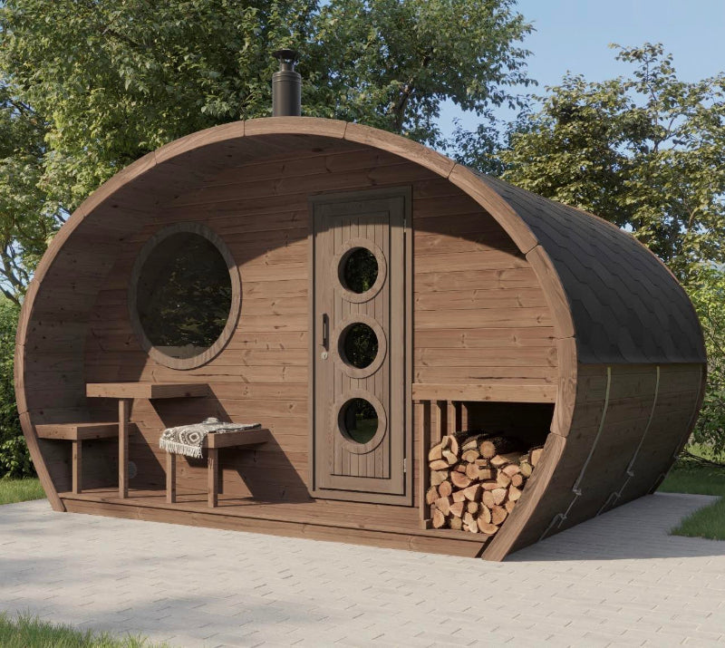 Dark-toned InMedias Oval Sauna Frodo 300 installed on a paved patio, featuring stacked firewood and circular windows , on a light gray and forest background.