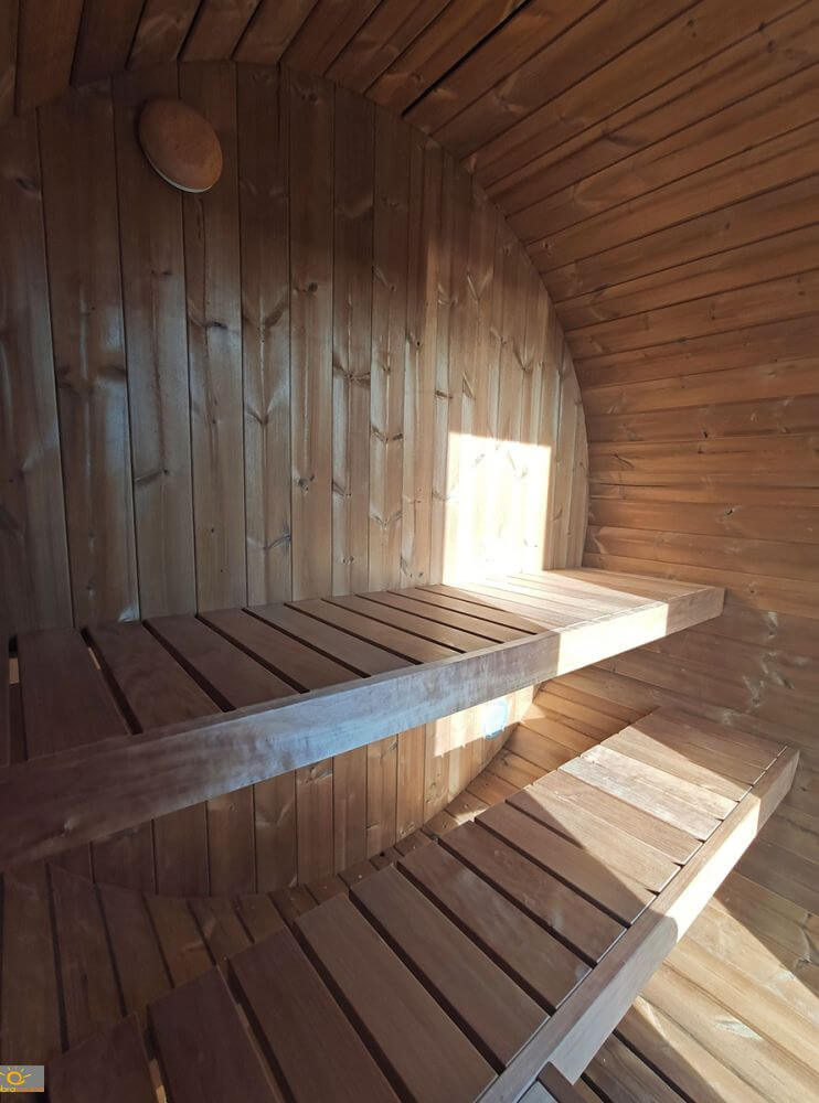 Inside the InMedias Terrace Sauna showing sunlit wooden benches curving with the barrel shape of the structure.