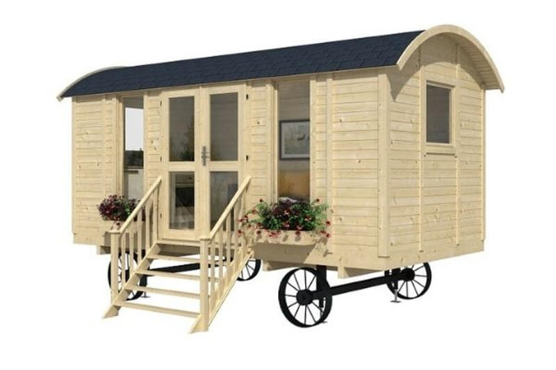 InMedias Modern Shepherd Hut in natural wood tone with black roof, featuring stairs, double glass doors, and flower boxes, on a white background.