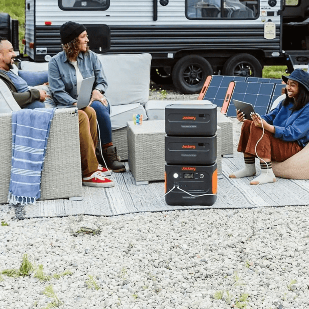 Jackery Explorer 1000 Plus in outdoor camping setup powering multiple devices, with people sitting near an RV.