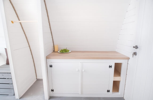 Viking Industrier 3.2 x 5.9m Camping Pod compact white kitchenette with wooden countertop and built-in storage on a white painted wood background.