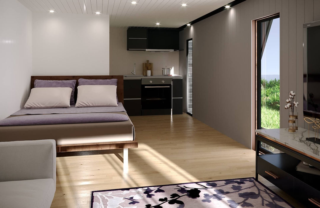 Modern glamping interior with visible bed, purple bedding, compact black kitchen, and natural wood flooring.