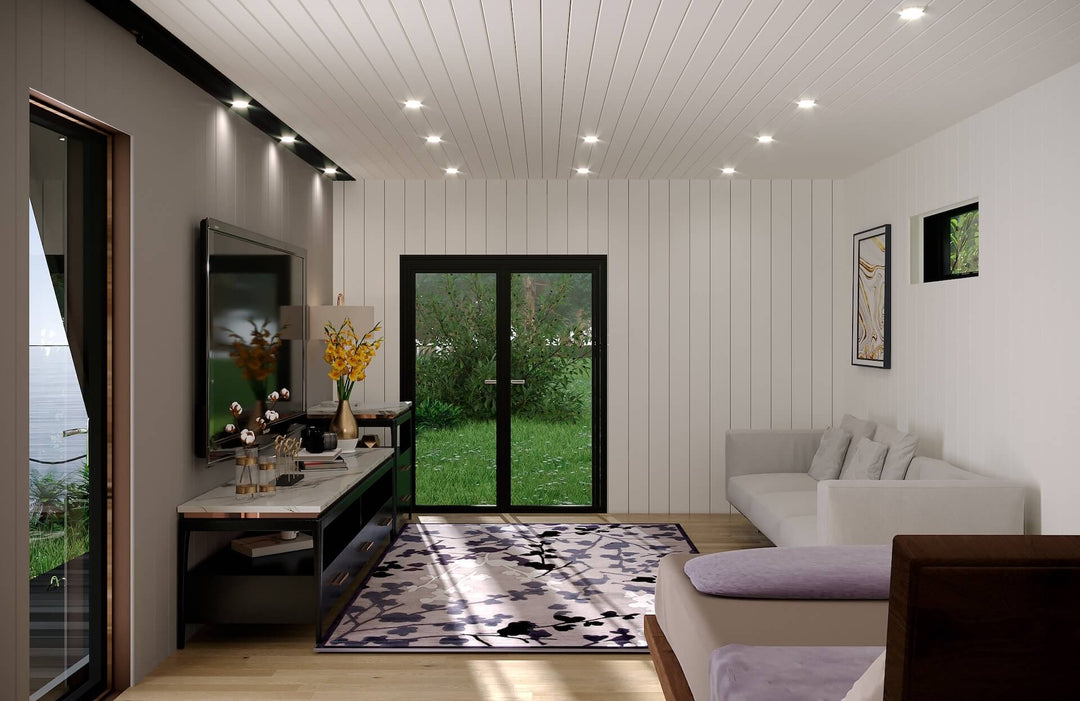 Interior of glamping unit featuring a white sofa, flat-screen TV, floral rug, and double glass doors opening to a grassy outdoor view.